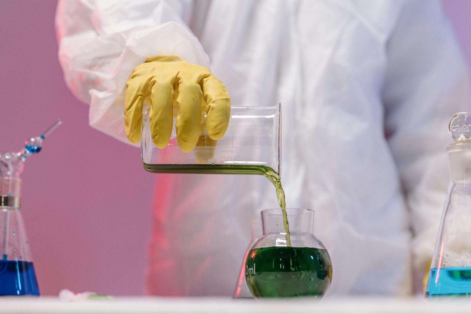 Scientist in protective gear pouring green liquid in a lab setting.